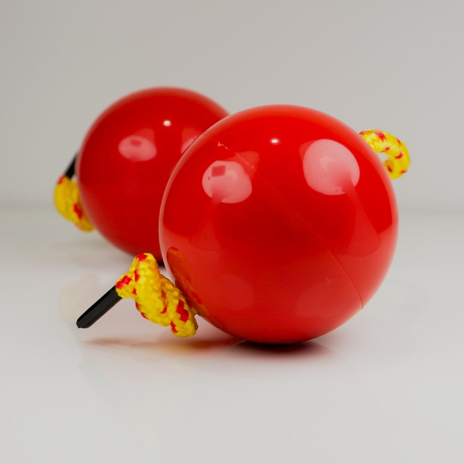 Two red sand balls with yellow strings on a light gray background