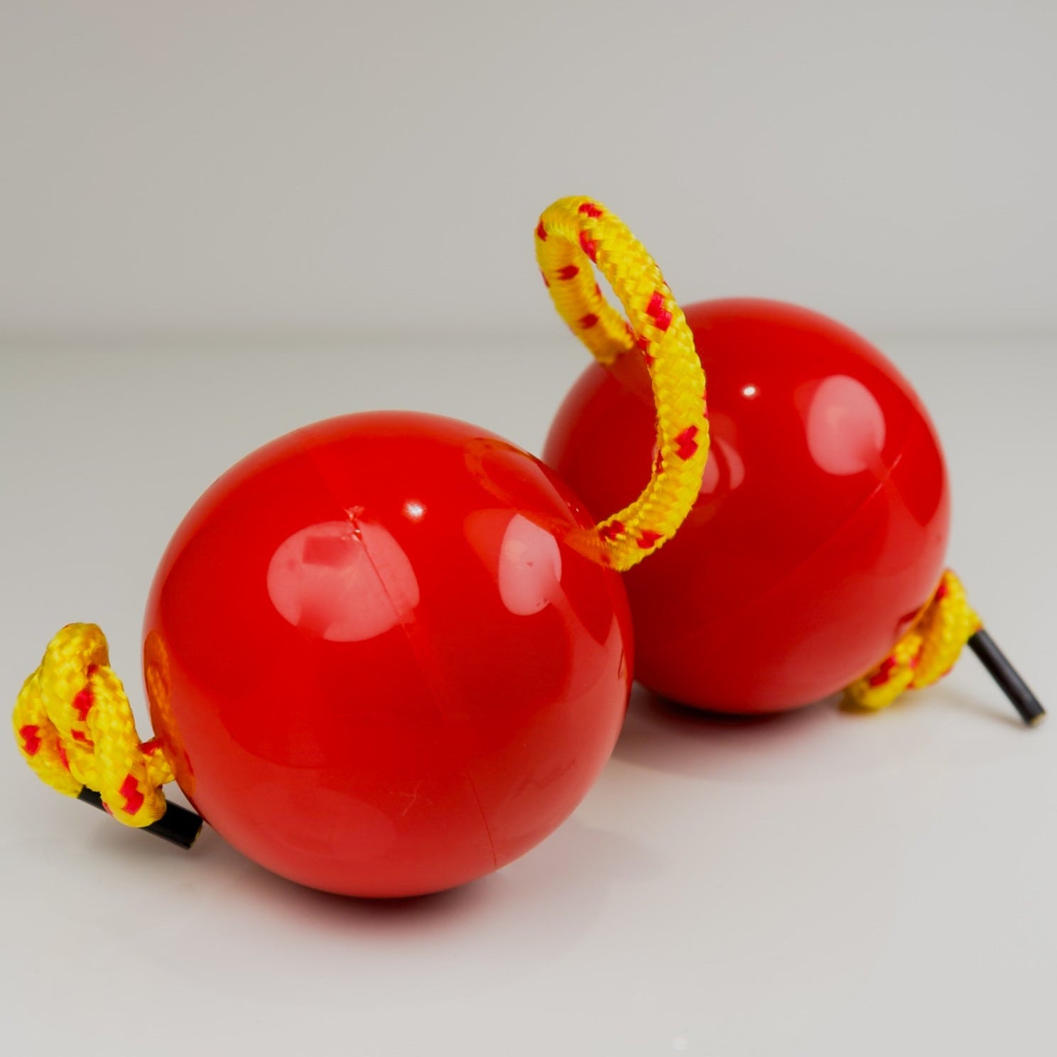 Two red sand balls with yellow strings on a light gray background