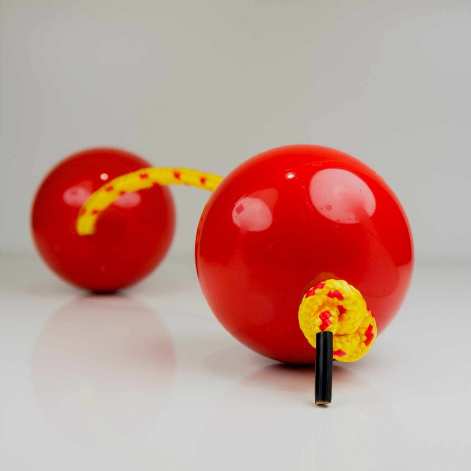 Two red sand balls with yellow strings on a light gray background
