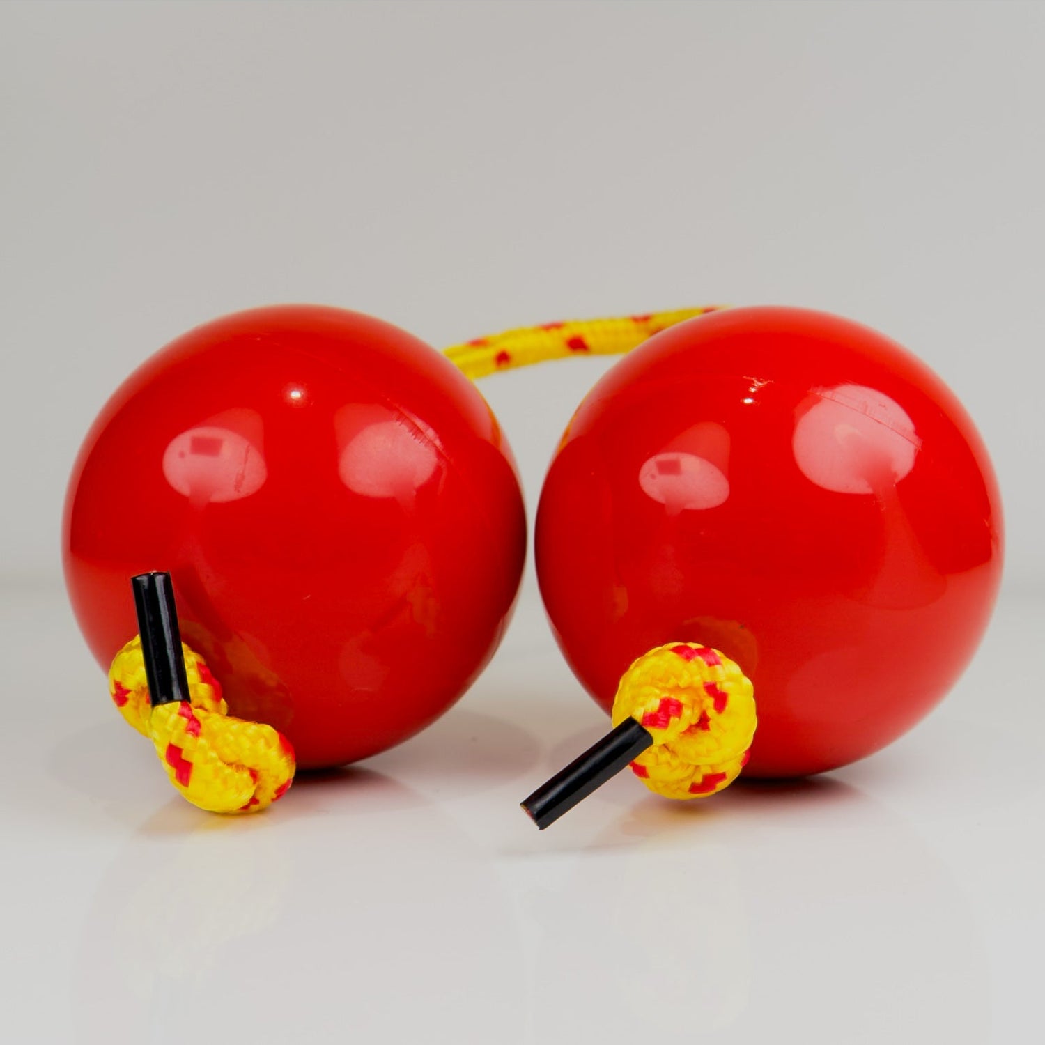 Two red sand balls with yellow strings on a light gray background