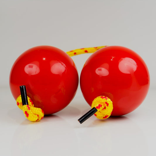Two red sand balls with yellow strings on a light gray background